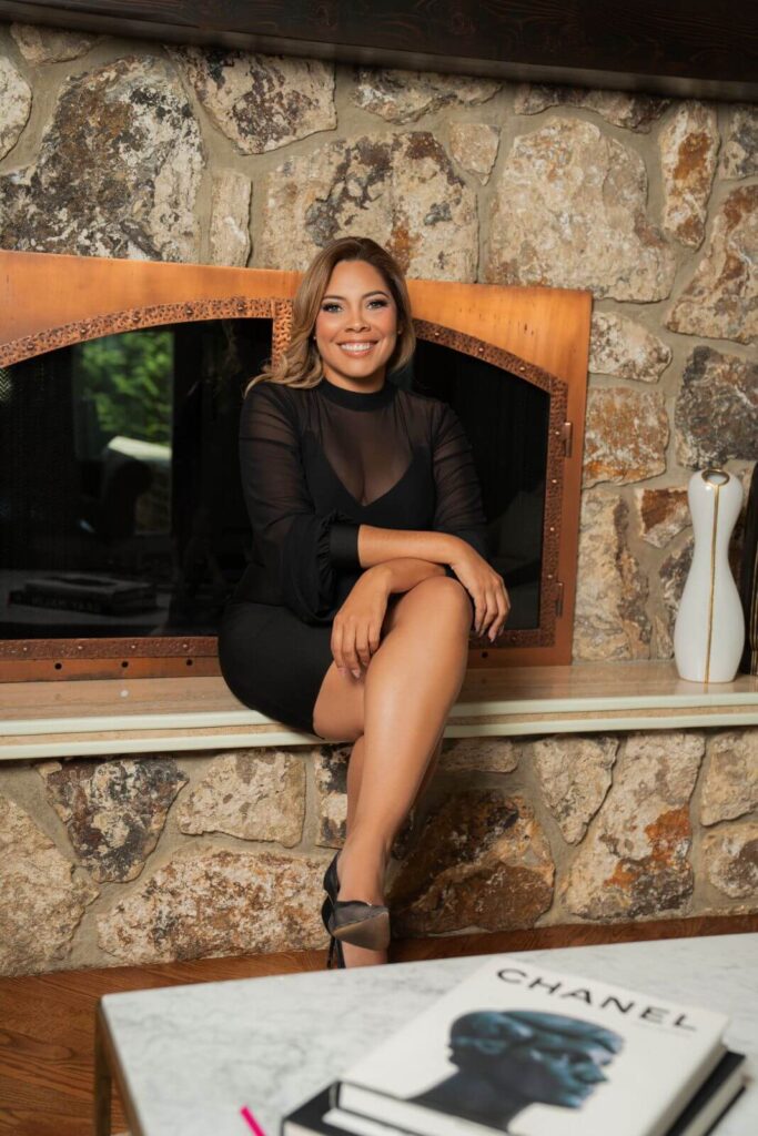 Interior designer Zamira Ariza seated beside the dramatic natural stone fireplace inside the completed Northern Velvet living room.