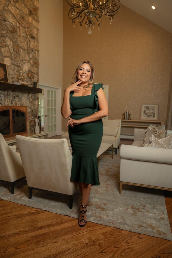 Interior designer Zamira Ariza standing inside the completed luxury living room featuring a dramatic stone fireplace and custom furnishings.